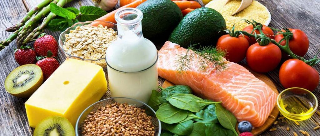A spread of food that includes salmon, cheese, kiwis, milk, tomatoes, asparagus, oats, avacadoes, and spinach